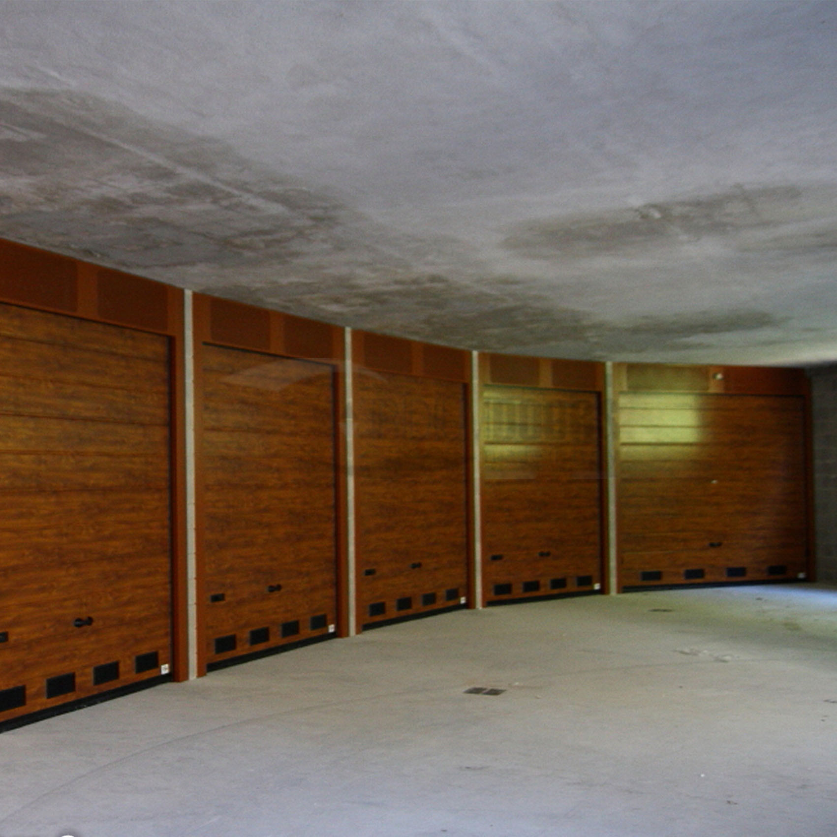 Portoni sezionali per condominio in tinta legno con velette a settori microforati verinicati e griglie di ventilazione in PVC nero Alba